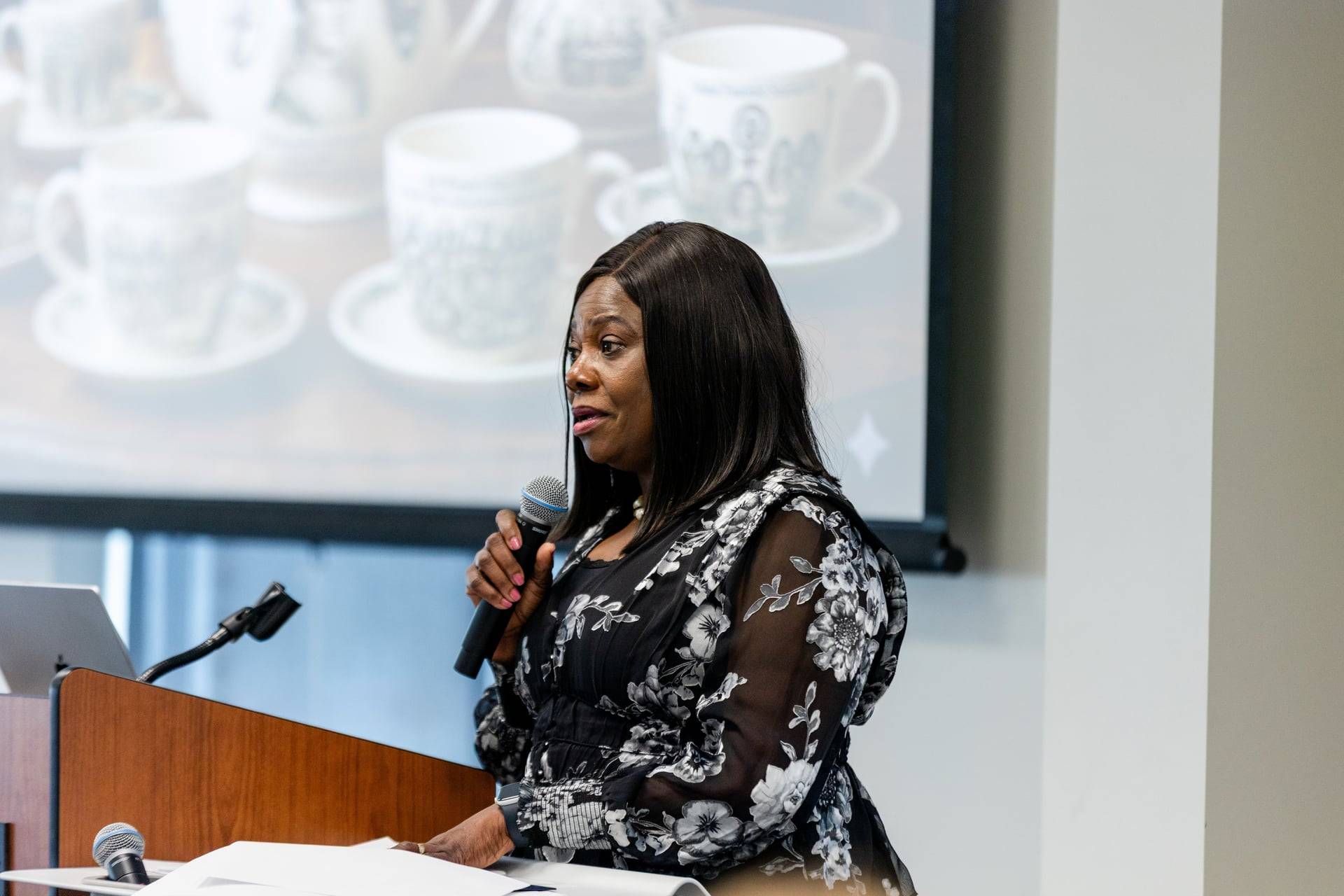 Photo shows Dr. Ronke Olawale with a microphone in front of a large screen giving her keynote presentation at EqualiTEA 2026